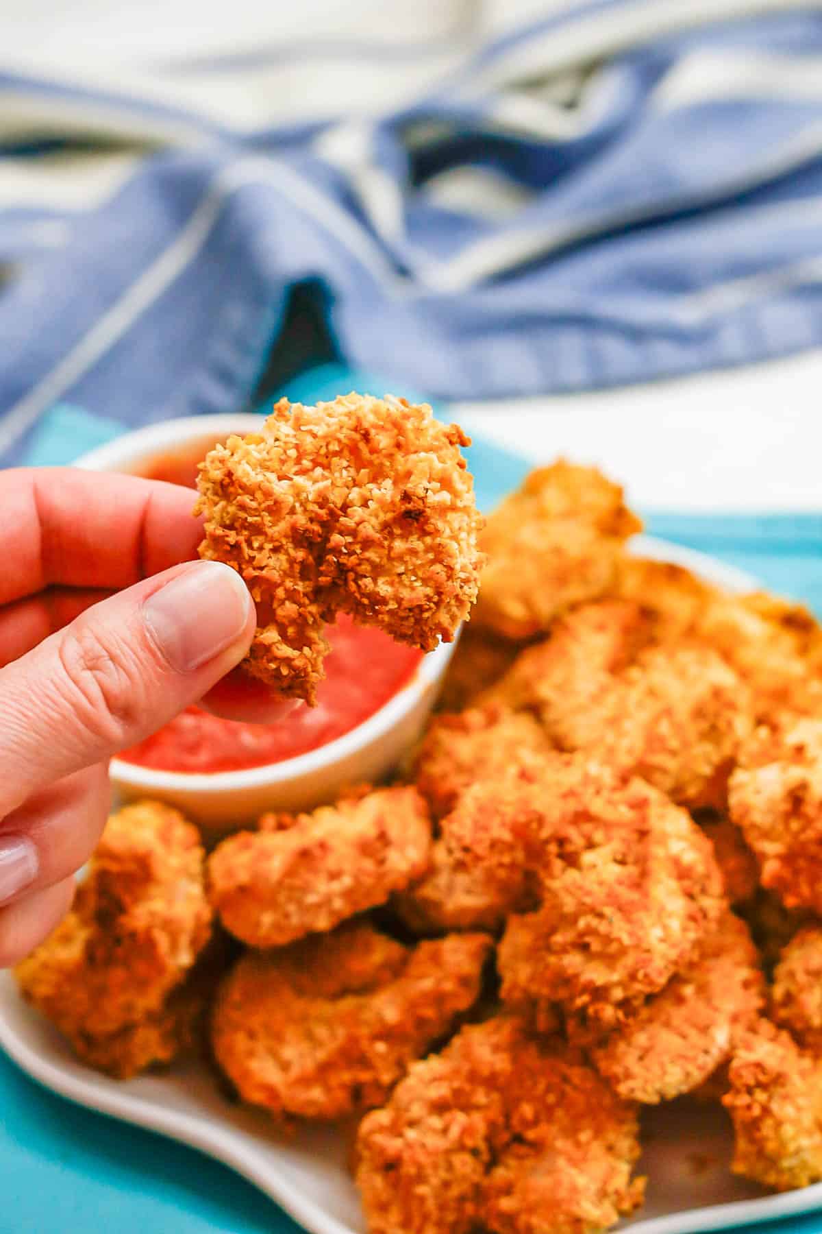 A hand holding up a crispy breaded shrimp.