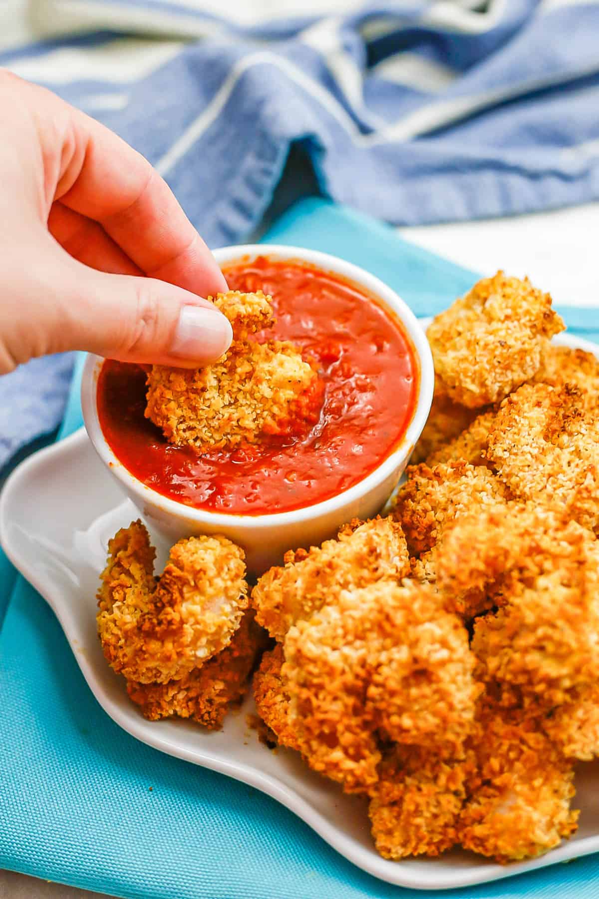 A hand dipping a coated shrimp into a small bowl of marinara sauce.