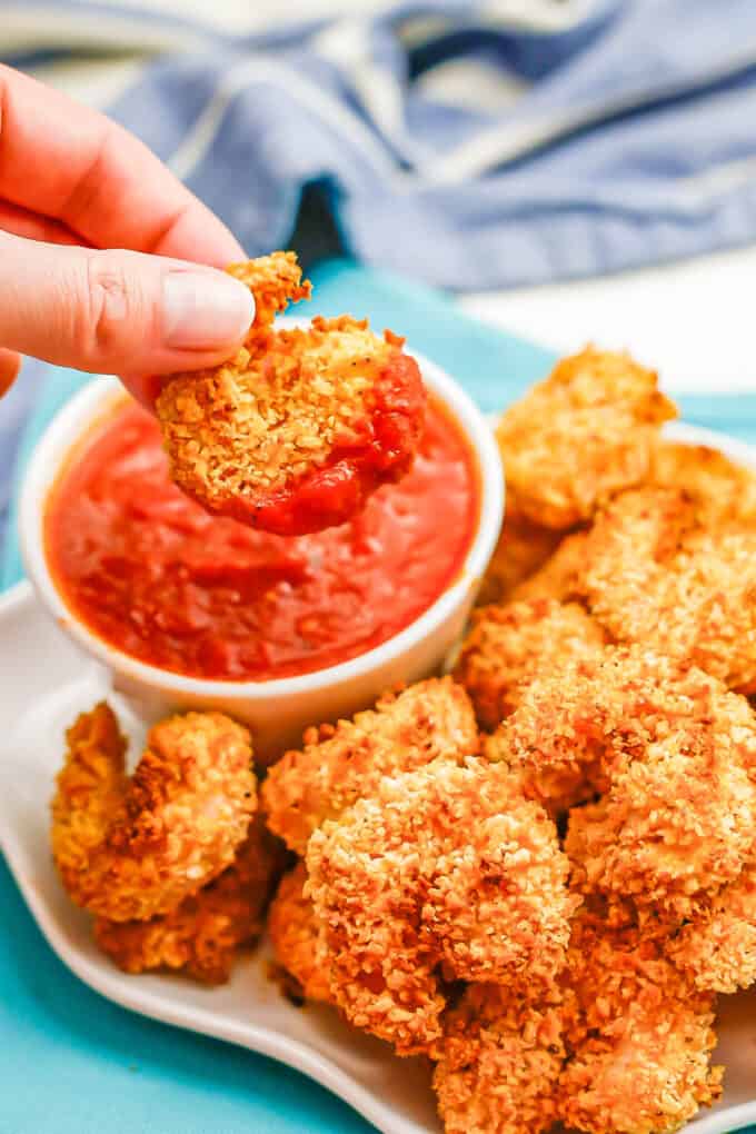 A hand holding a piece of breaded shrimp dipped in marinara sauce.