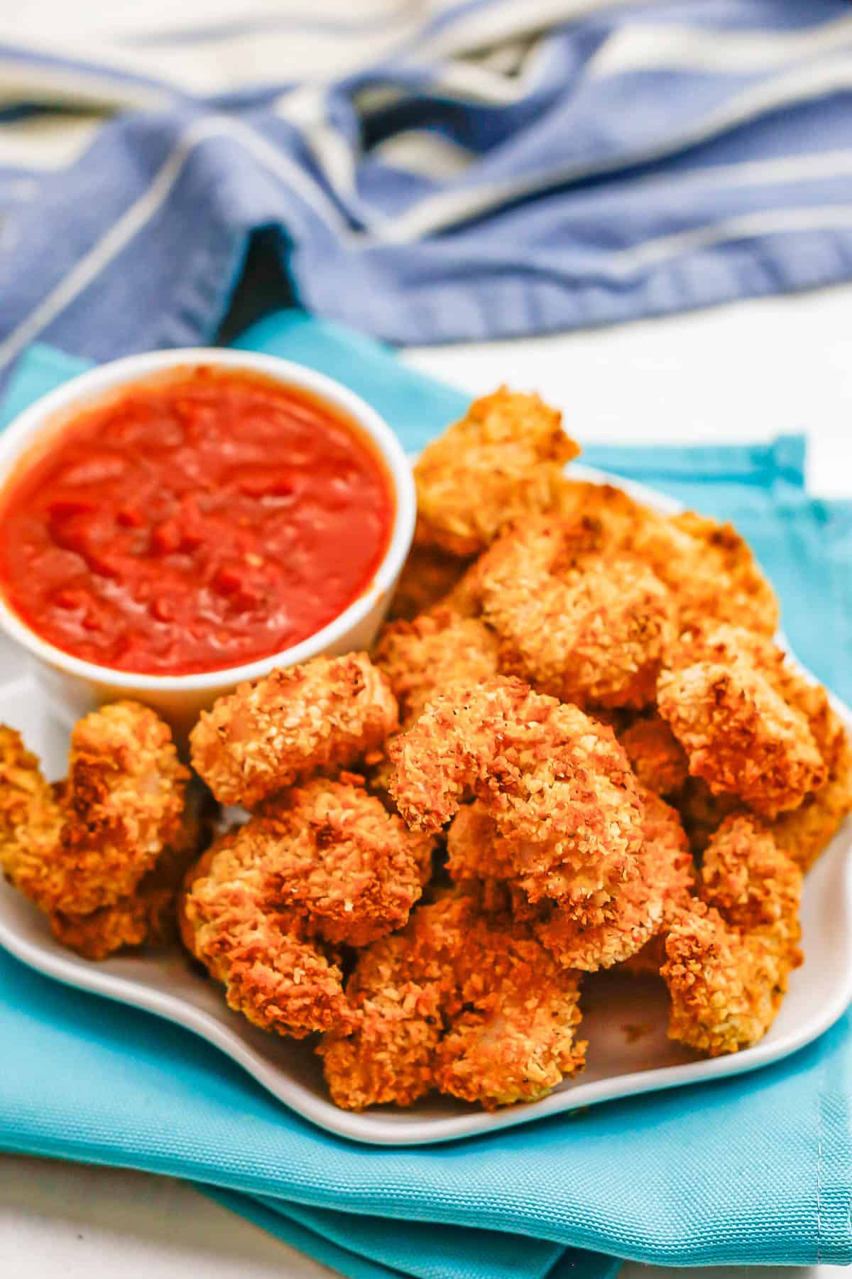 Breaded shrimp piled on a white plate alongside a small bowl of marinara sauce for dipping.