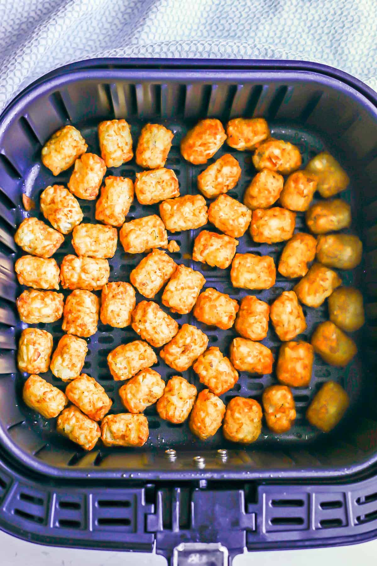 An Air Fryer with cooked tater tots in an even layer.