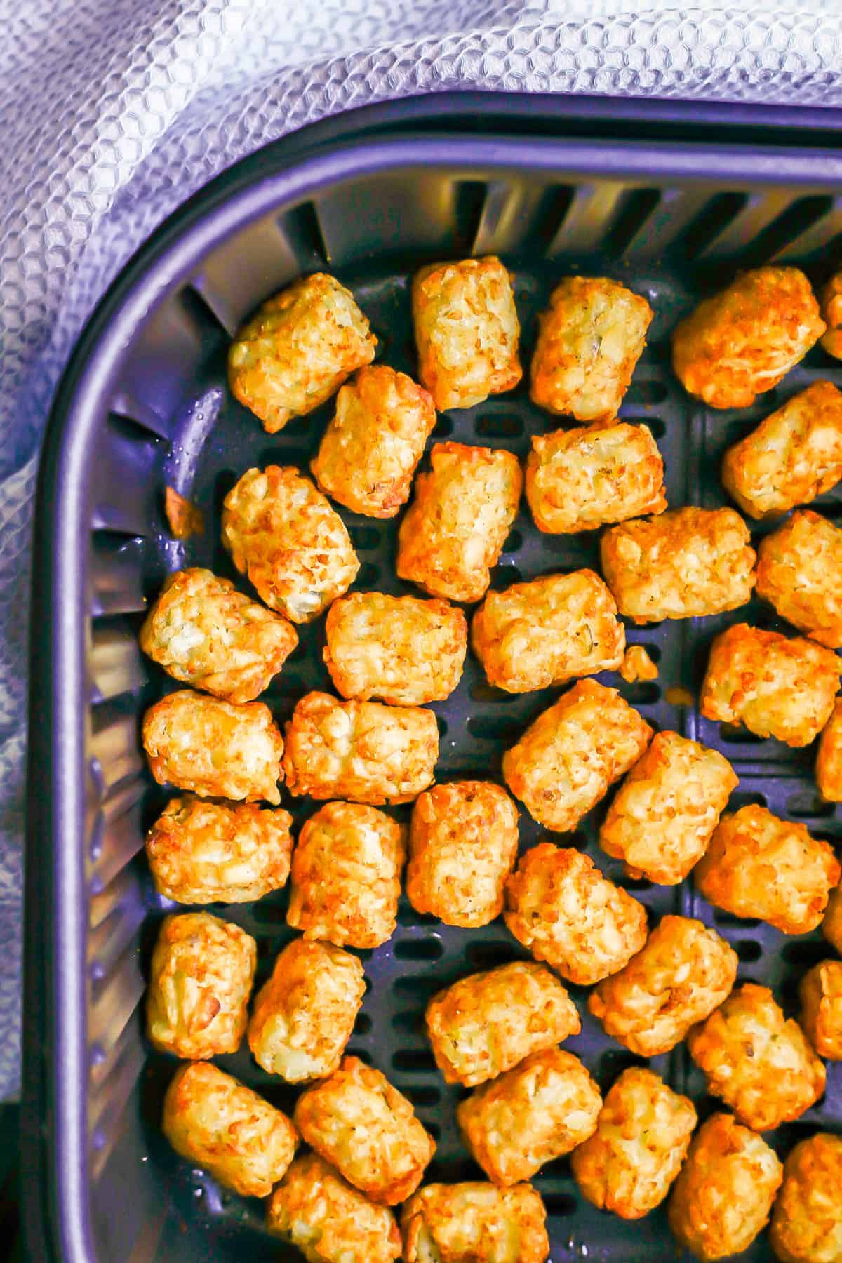 Air Fryer tater tots with a blue towel to the side.