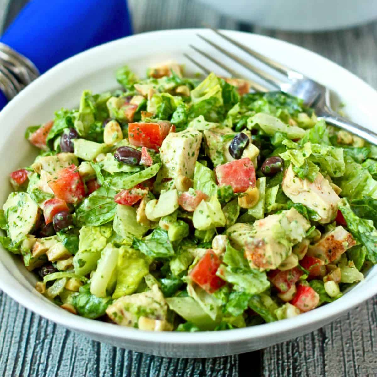 A white bowl with a colorful chopped southwestern salad with chicken, black beans, veggies and a creamy cilantro lime dressing.