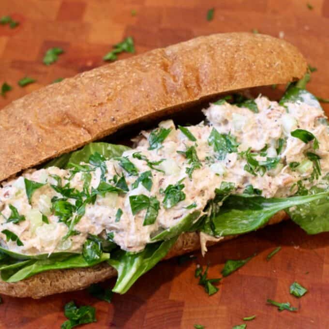 Close up of a crab salad sandwich on a long whole wheat hoagie roll with fresh chopped parsley sprinkled on top and to the side.