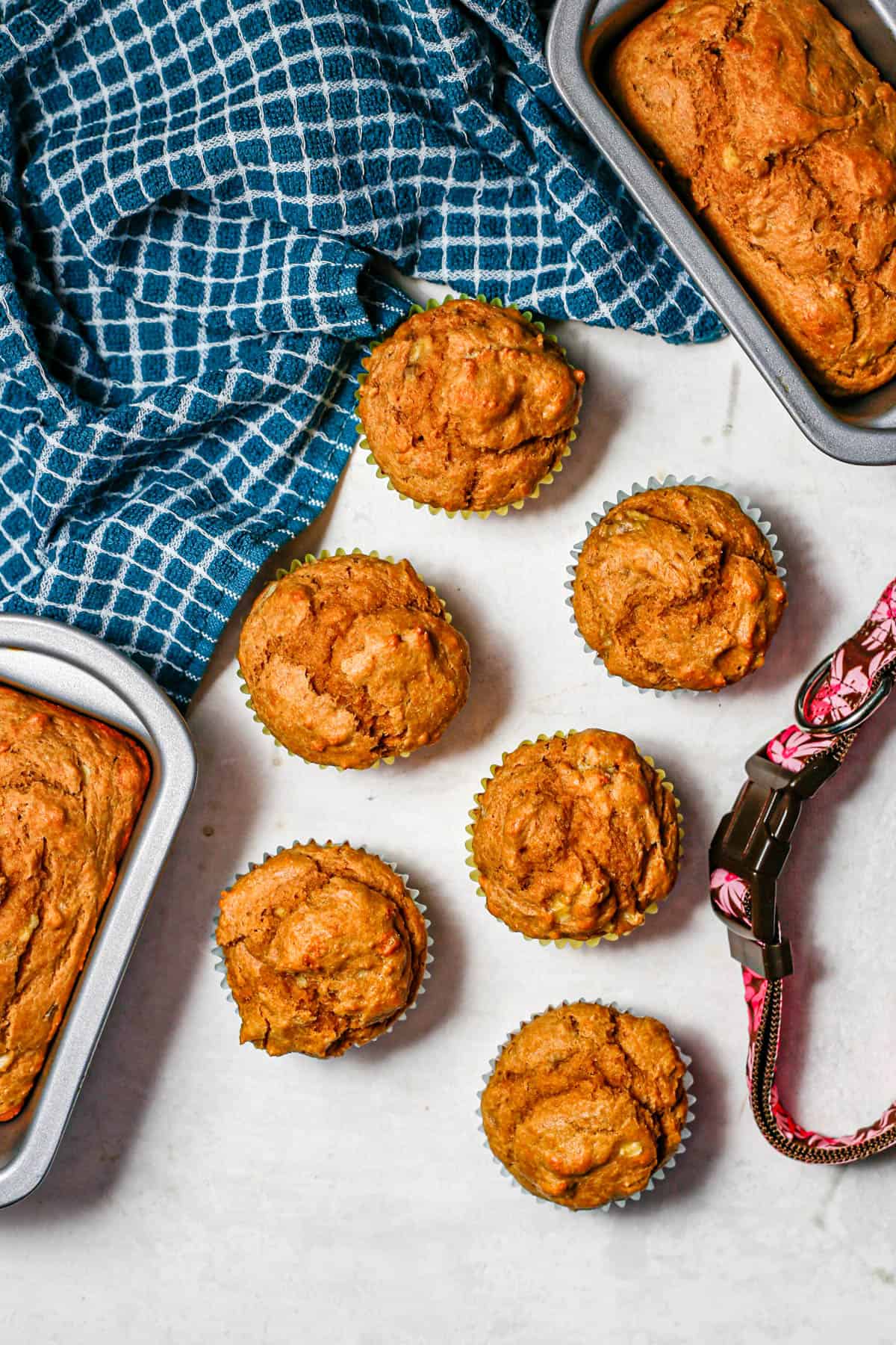 Muffins and mini loaf pans of dog cakes on a counter beside a dog collar.