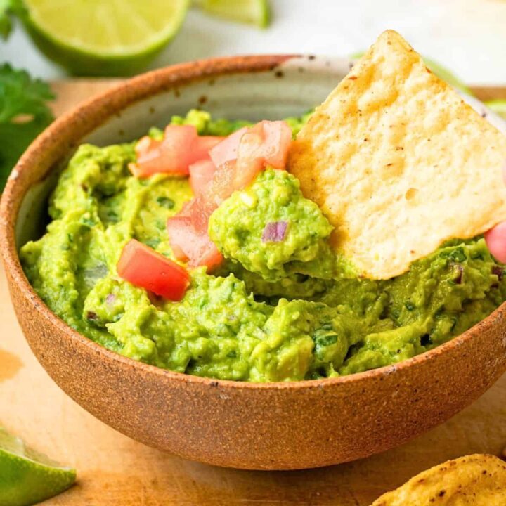 Close up of a chip scooping up some guacamole from a serving bowl.