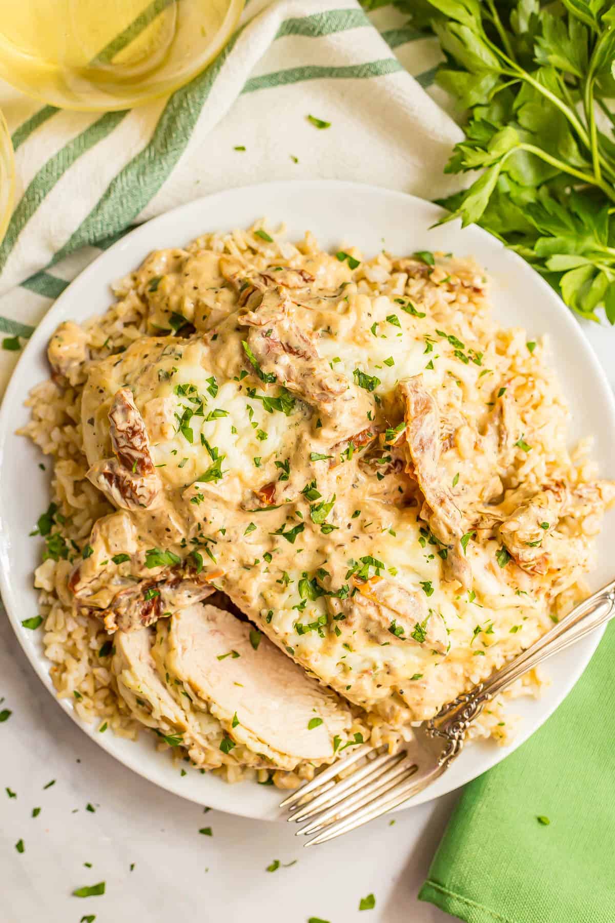 A fork resting on a white plate of a sliced creamy Italian chicken breast served over rice.