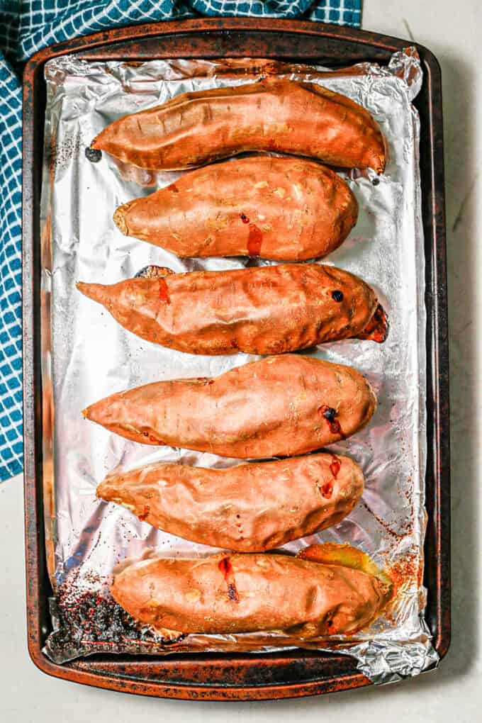 Baked sweet potatoes on a foil lined baking sheet.