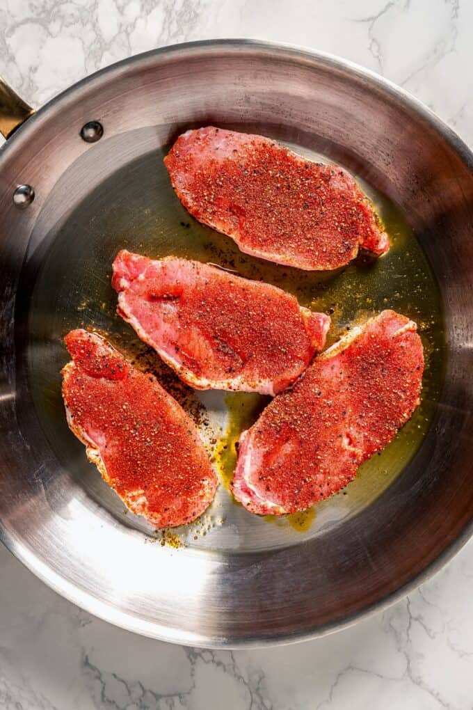 Seasoned pork chops being seared in a large skillet.