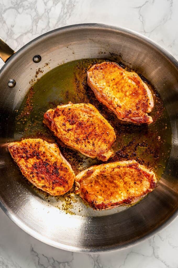 Seasoned seared pork chops in a large silver skillet.