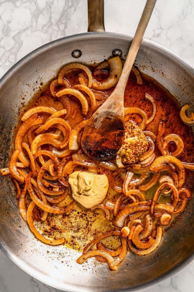Sautéed onions with broth and mustard being mixed together for a sauce in a large skillet.