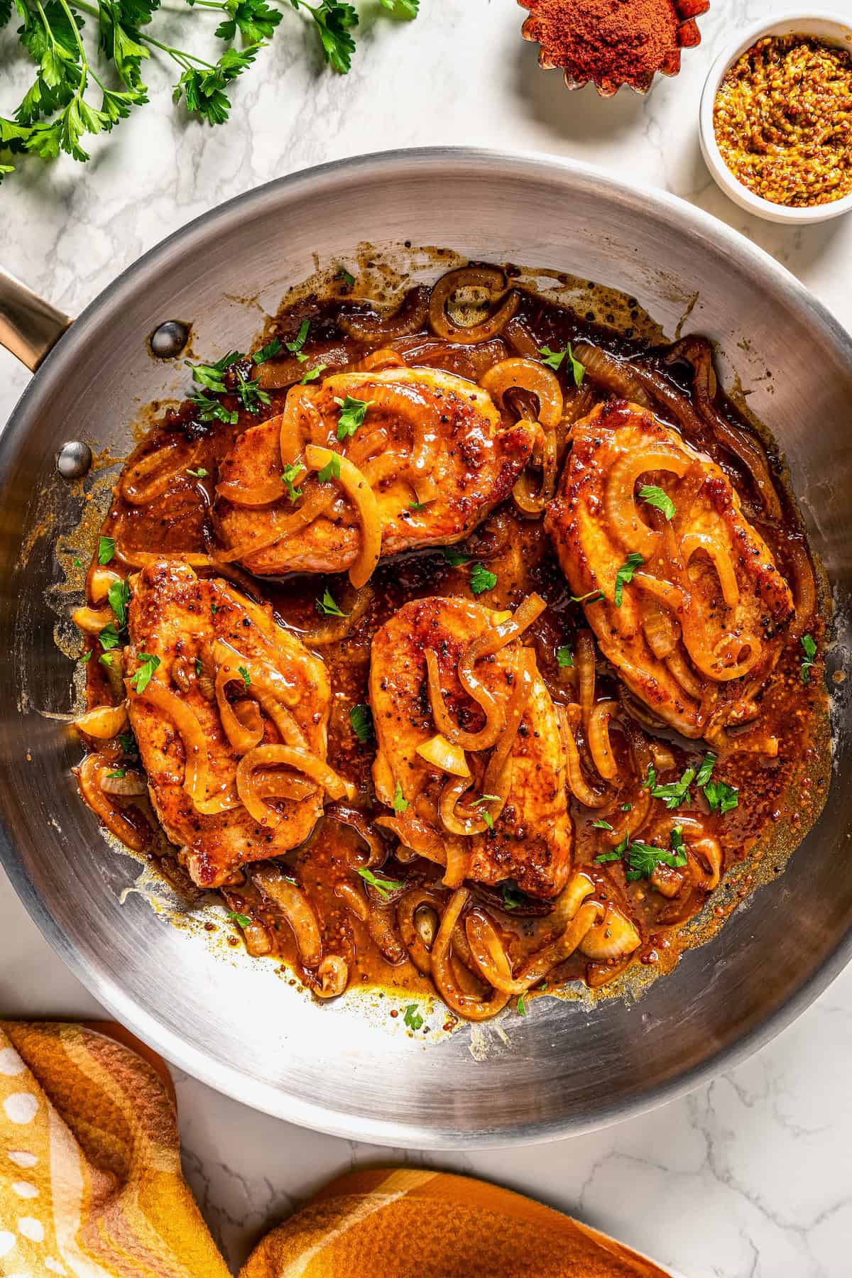 Honey mustard pork chops with onions and fresh parsley in a large skillet.