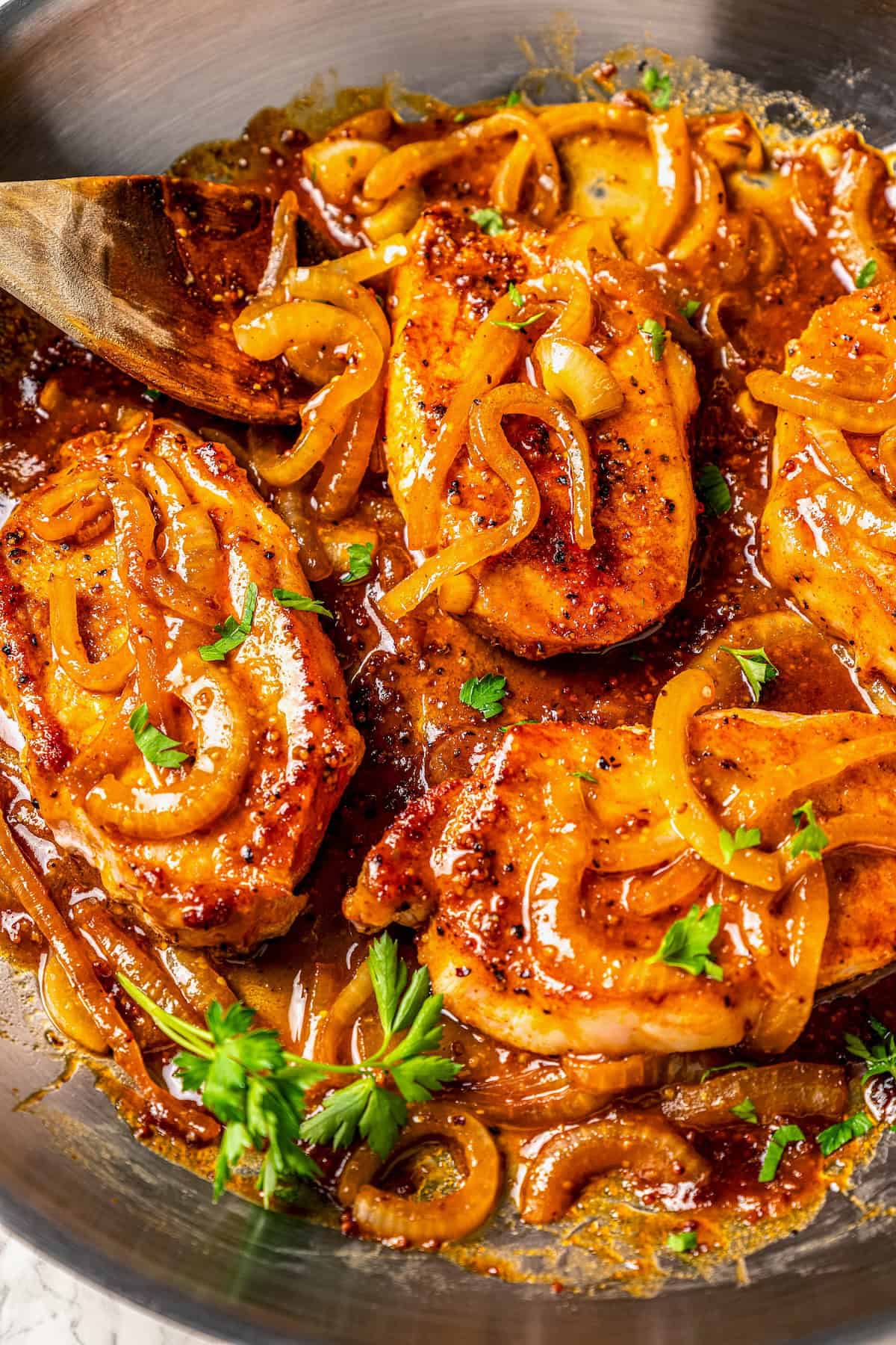 Close up of honey mustard pork chops with onions and fresh parsley in a large skillet.