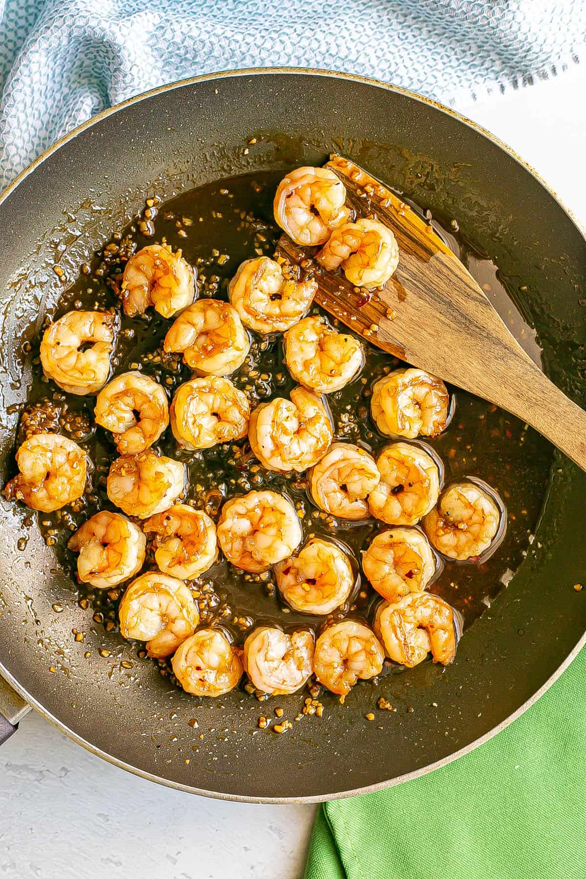 Cooked shrimp in a honey garlic sauce in a large skillet with a wooden spatula resting in it.