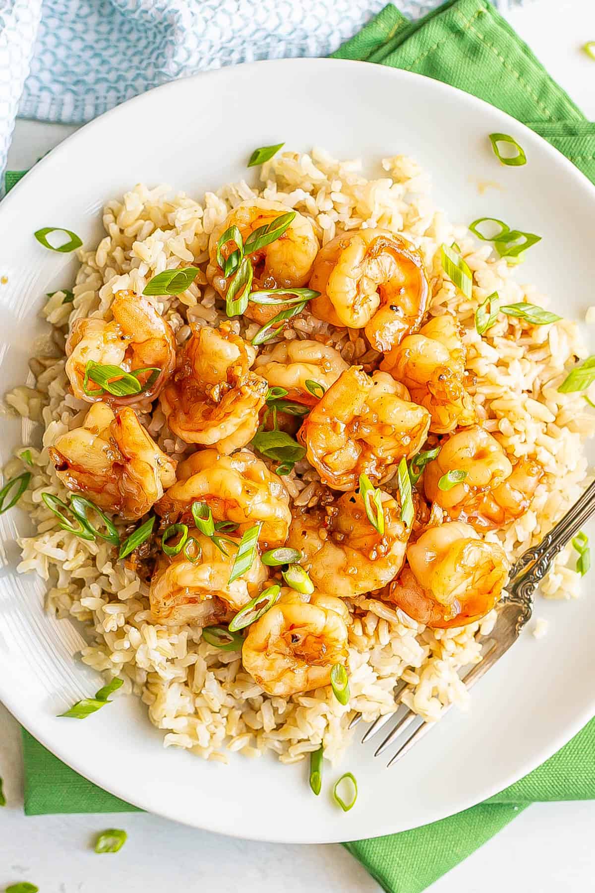 Honey garlic shrimp served on top of steamed brown rice on a white plate with sliced green onions sprinkled on top.