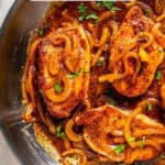 Close up of pork chops in a large skillet with sautéed onions and honey mustard sauce and a text overlay on the photo.