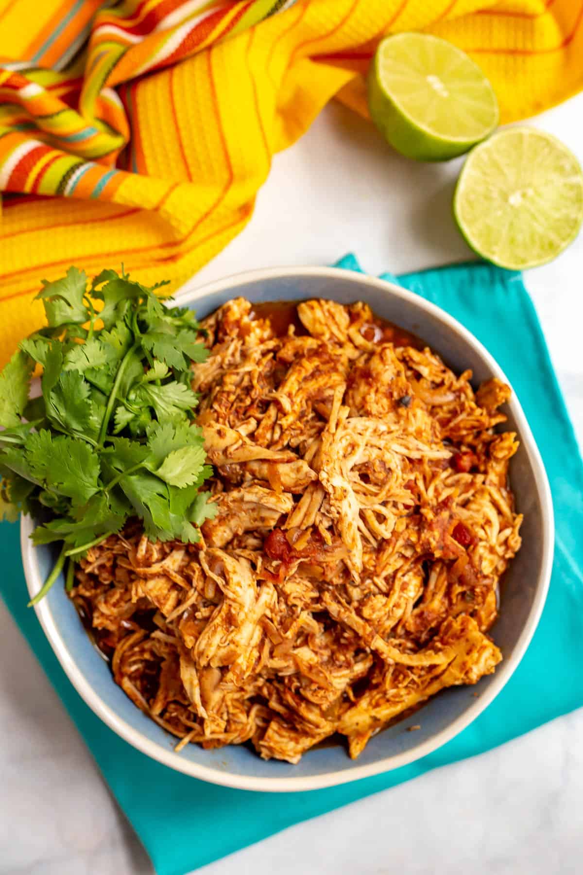 Shredded Mexican style chicken in a blue and white bowl with cilantro for a garnish and a halved lime nearby.