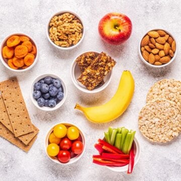 An assortment of healthy snacks arranged on a counter, including nuts, fruit, rice cakes and graham crackers.