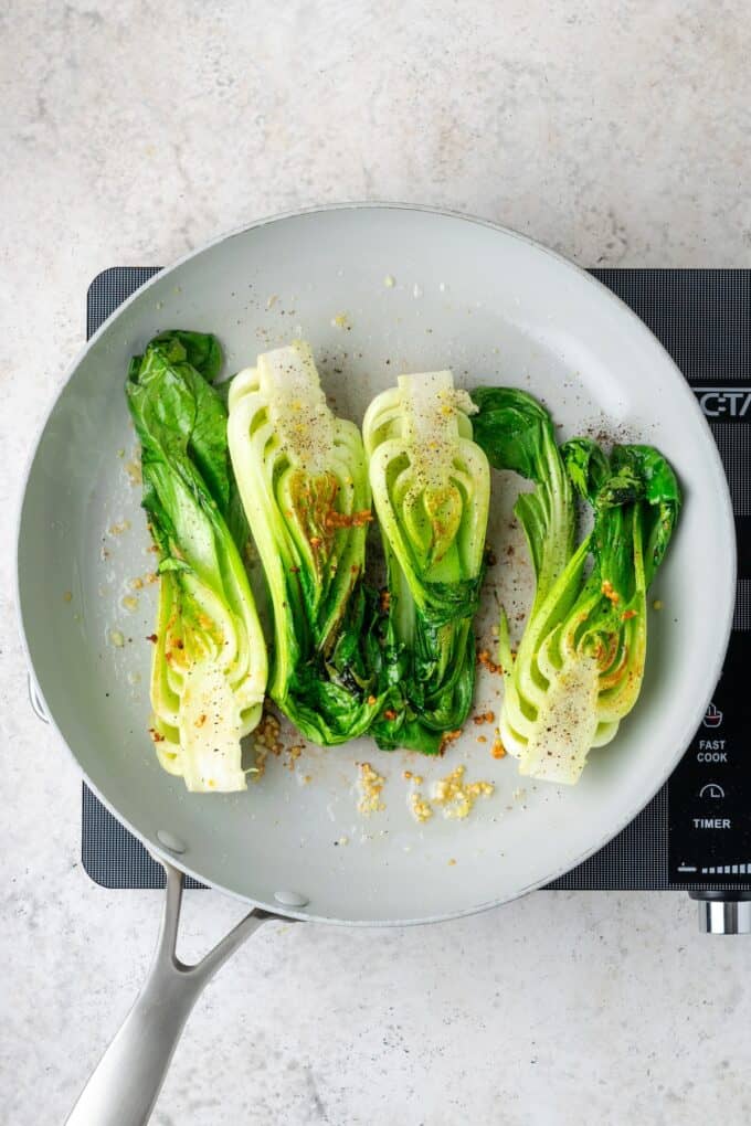 Seasoned and seared bok choy in a large skillet with garlic and ginger.