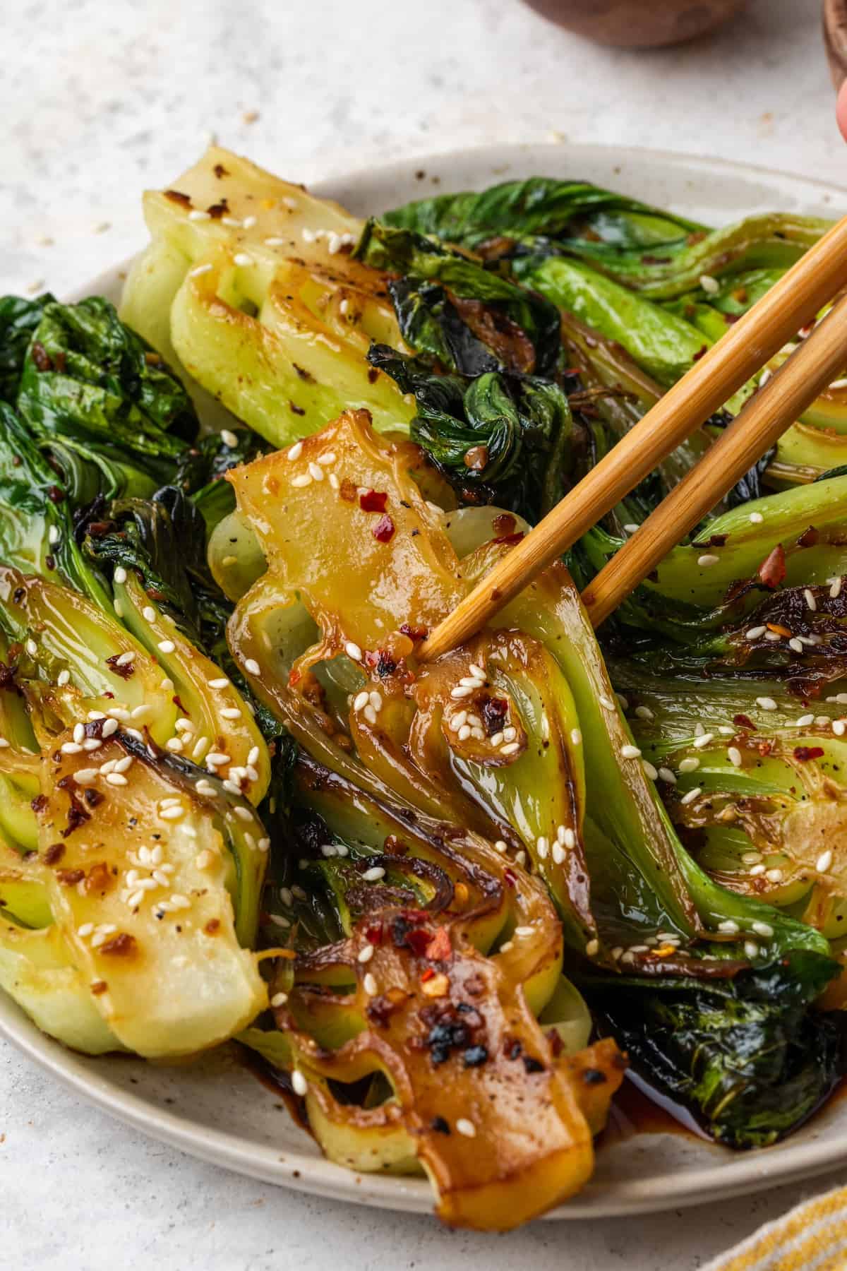 Chopsticks starting to pick up a piece of bok choy from a serving platter.