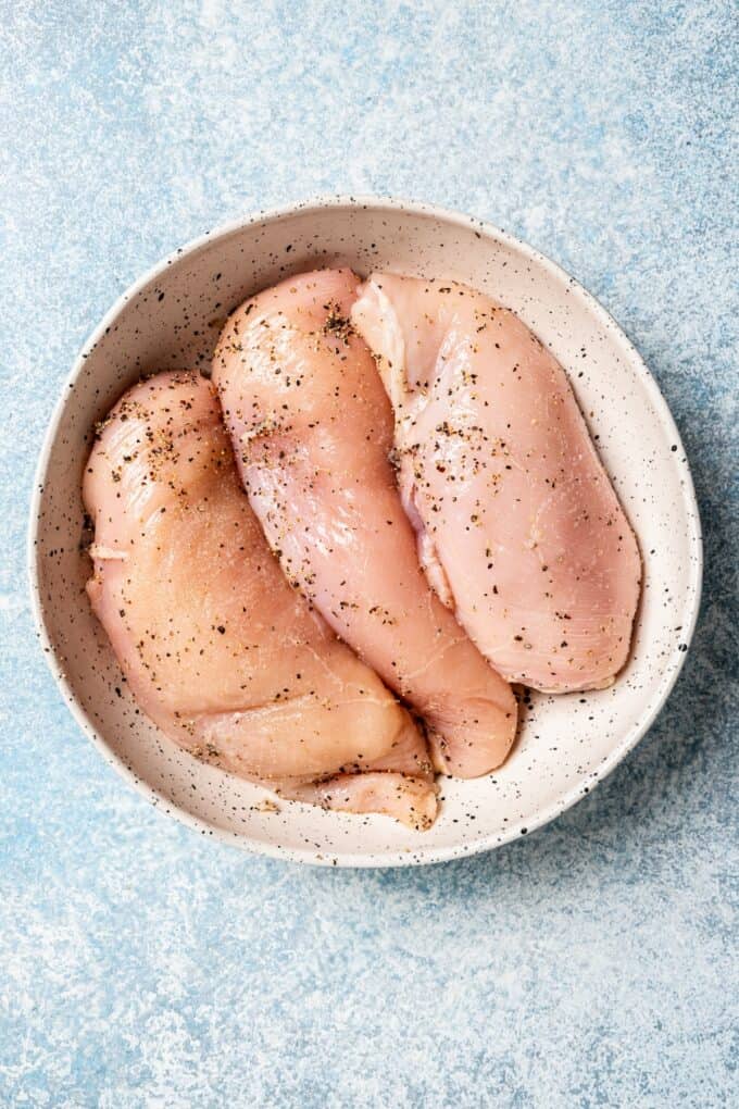 Seasoned raw chicken breasts in a bowl.