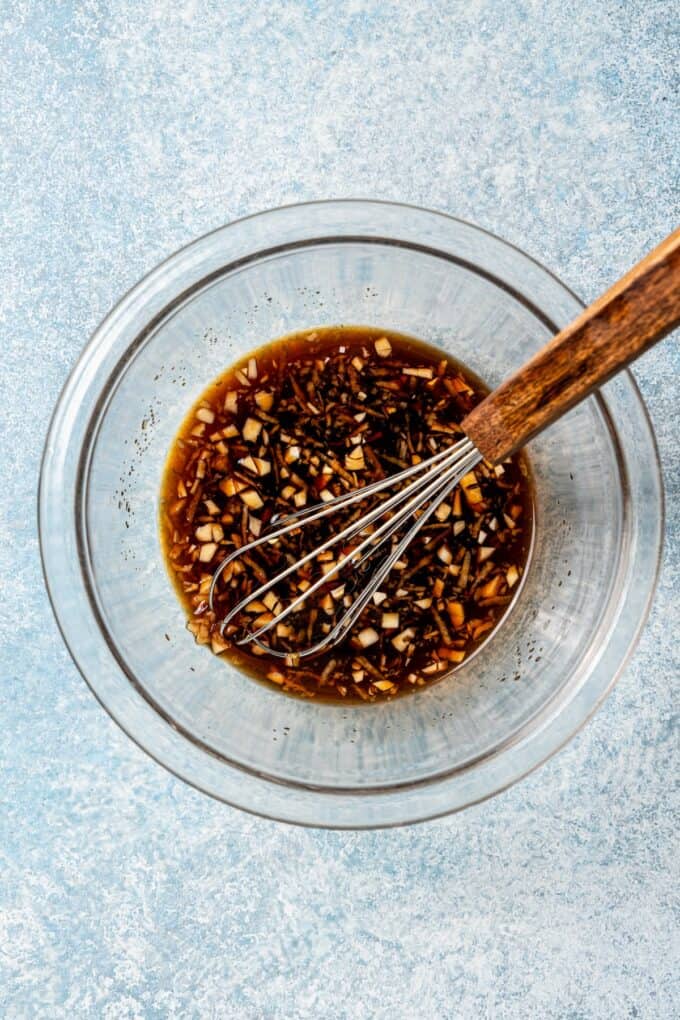A clear glass bowl with a soy sauce mixture and a whisk resting in the bowl.