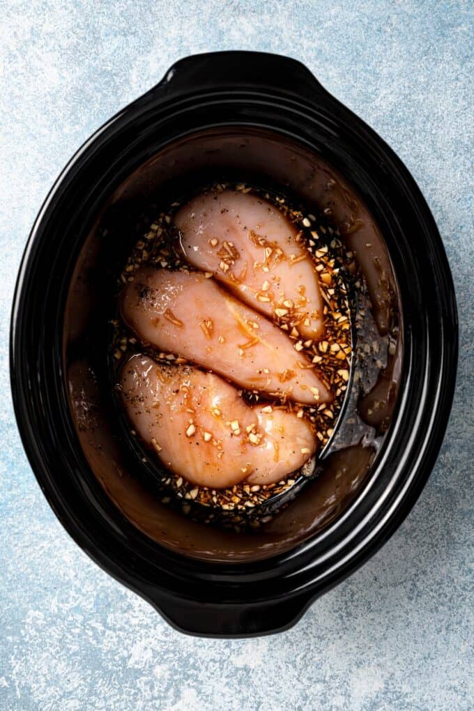 A black slow cooker with a bourbon chicken mixture in it before being cooked.