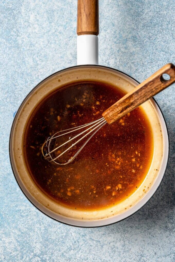 A small sauce pan with a bourbon soy sauce mixture being reduced and a whisk resting in the pan.
