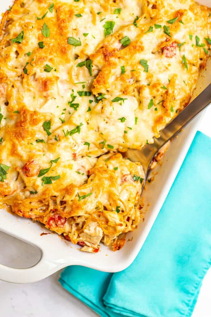 A serving spoon scooping up some baked chicken spaghetti from a large white casserole dish.