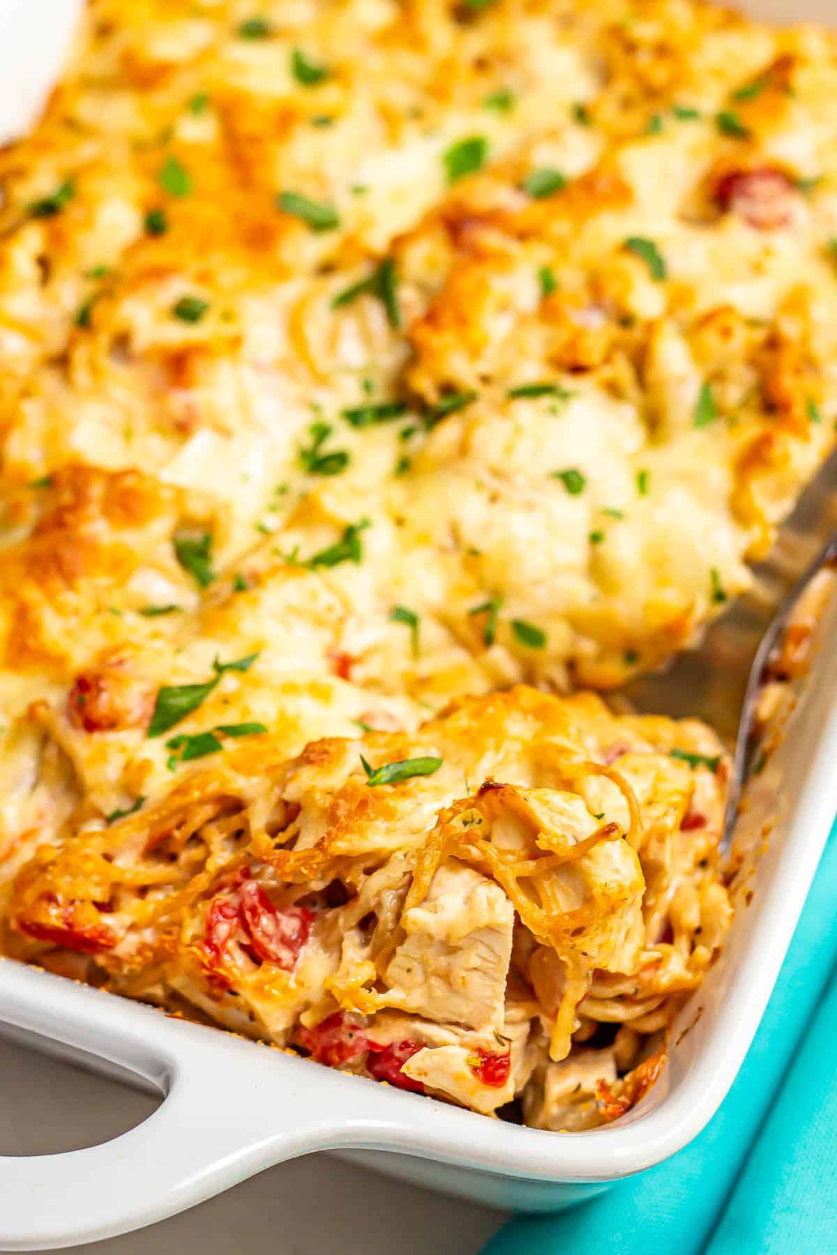 A scoop of baked chicken spaghetti being lifted from a large white casserole dish.