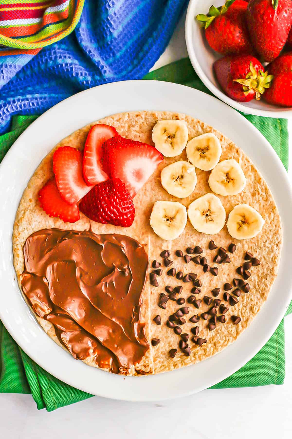 A folded wrap tortilla for dessert with quadrants of nutella, sliced strawberries, sliced bananas and mini chocolate chips.