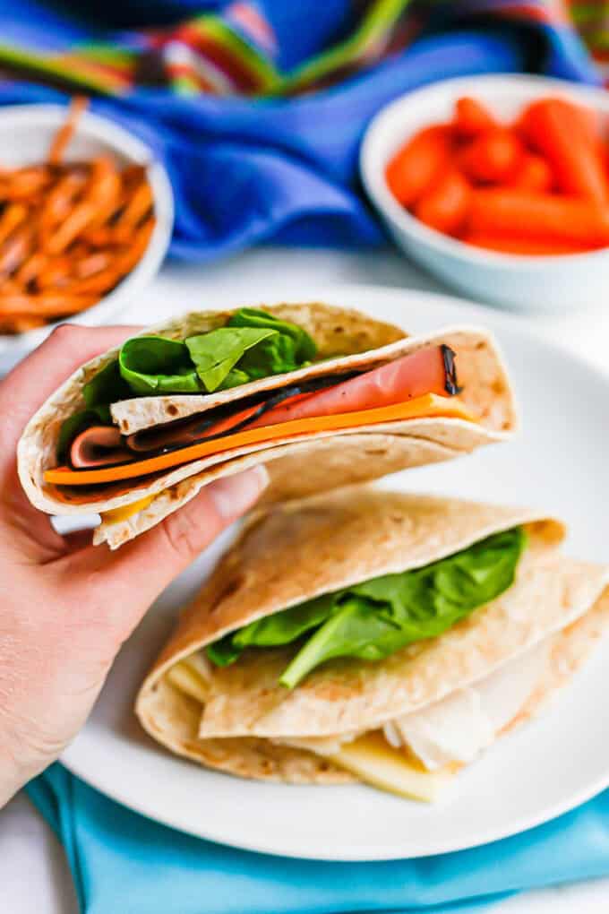 A hand holding a folded wrap sandwich with ham and cheddar cheese.