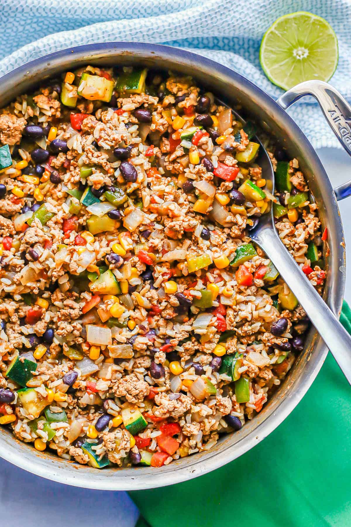 A spoon resting in a large pot with a mixture of ground turkey, rice, beans and veggies.