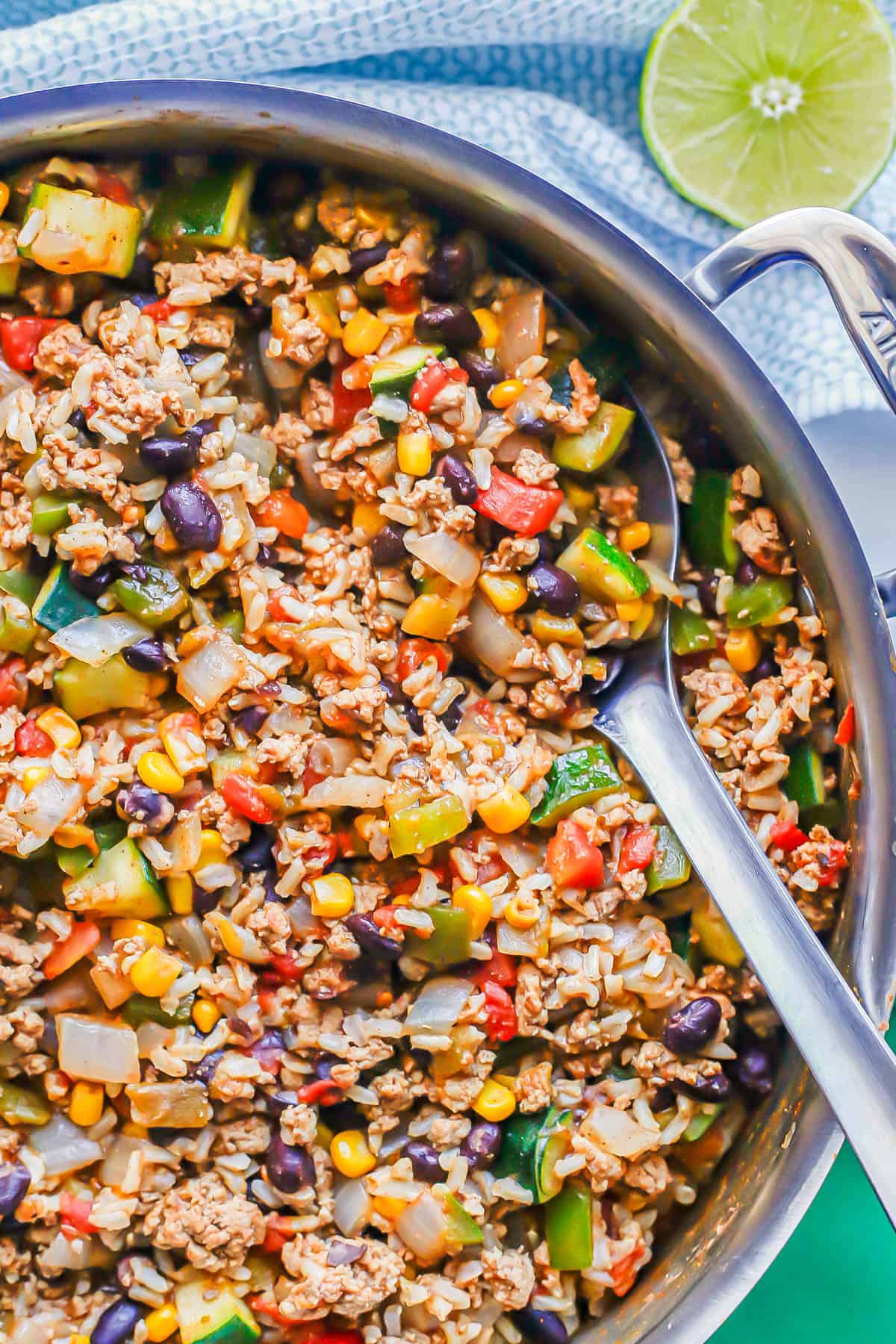 A silver serving spoon resting in a large pot with a mixture of ground turkey, rice, beans and veggies.