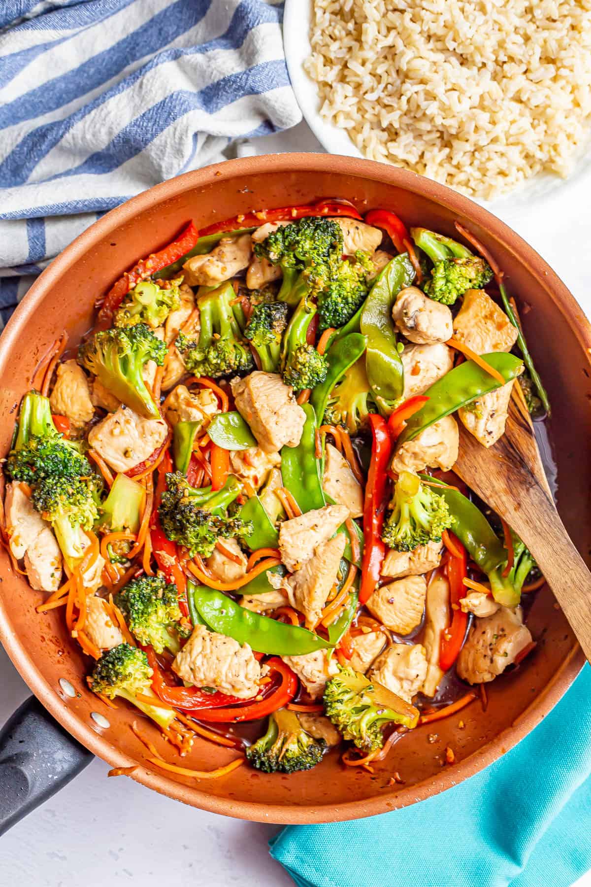 A large copper skillet with a chicken and vegetable stir fry and a bowl of rice to the side.