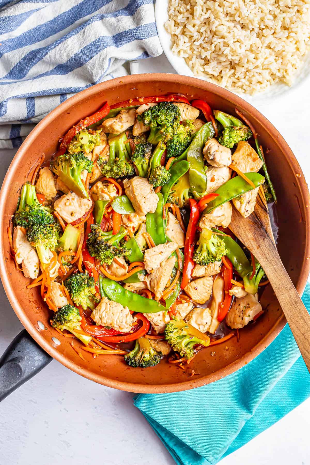 Chicken and veggie stir fry with a honey garlic sauce in a large skillet with a wooden spoon resting in it.