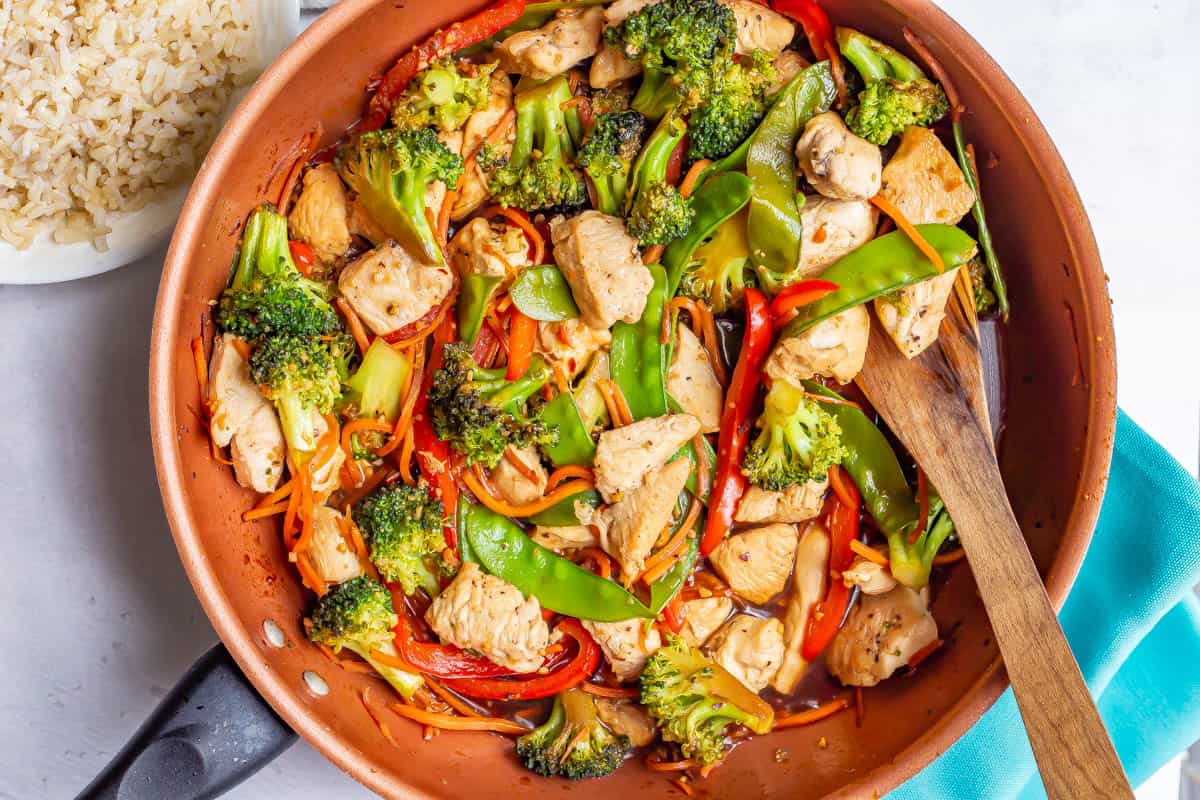 Honey garlic chicken stir fry in a large copper skillet with a wooden spatula resting in it.