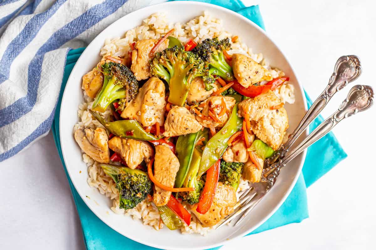 A low white bowl with rice topped with a stir fry mixture of chicken and vegetables.