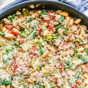 Close up of a ground turkey skillet with white beans, spinach, tomatoes and Parmesan cheese on top.