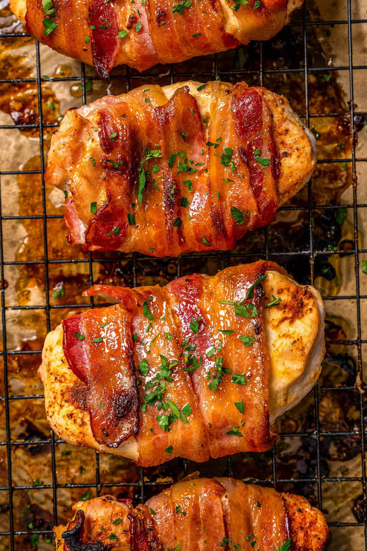Close up of roasted bacon wrapped chicken breasts on a wire rack set on a baking pan with parsley sprinkled on top.