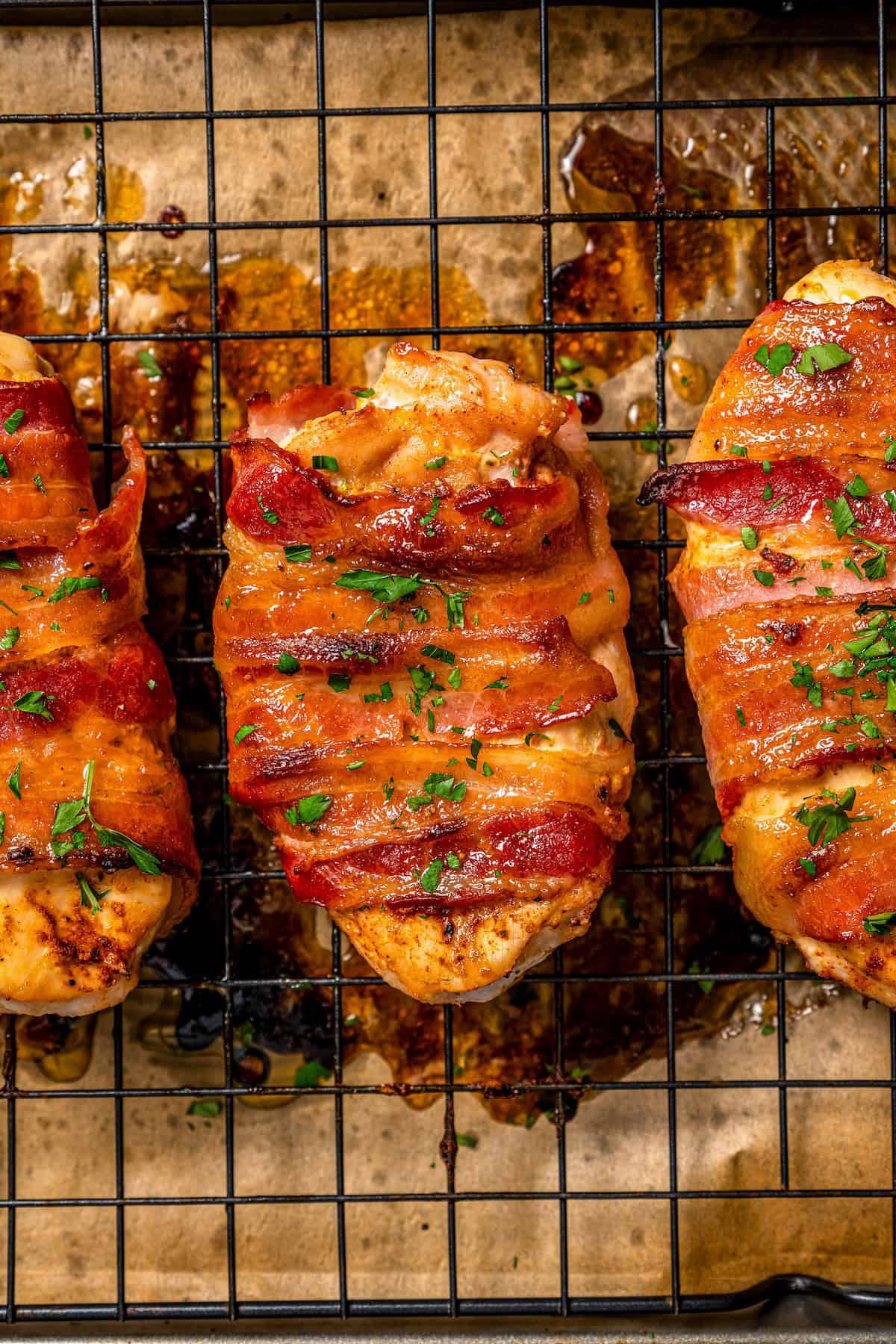 Roasted bacon wrapped chicken breasts on a wire rack set on a baking pan with parsley sprinkled on top before being served.