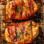 Close up of roasted bacon wrapped chicken breasts on a wire rack set on a baking pan with parsley sprinkled on top and a text overlay on the photo.