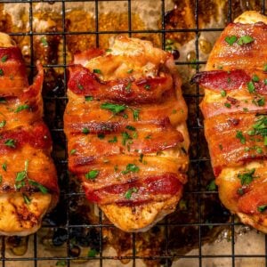 Close up of roasted bacon wrapped chicken breasts on a wire rack set on a baking pan with parsley sprinkled on top before being served.