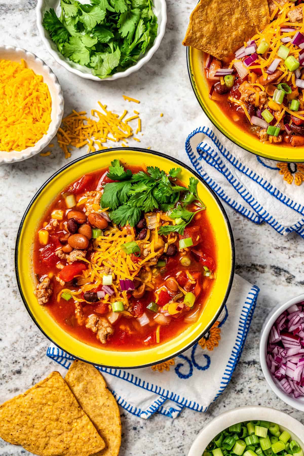 A bowl of taco soup with bowls of toppings nearby.