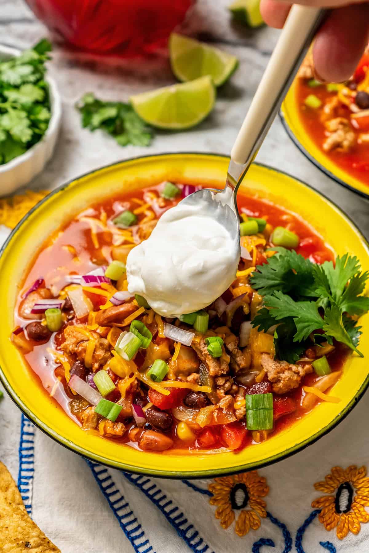 A spoon dolloping some sour cream on a bowl full of taco soup.