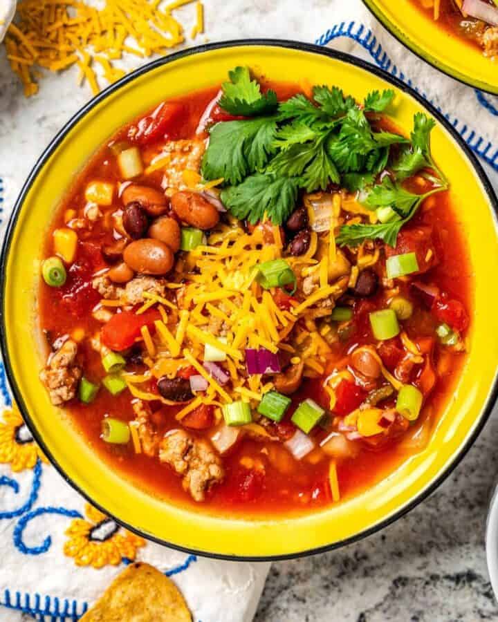 Close up of a bowl full of taco soup with cheese and cilantro on top and additional toppings in bowls to the side.