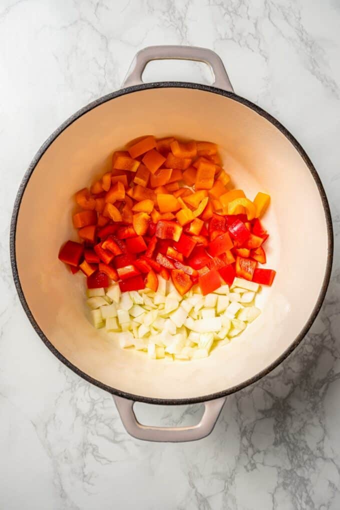 Onions and bell peppers in a large pot before being cooked.