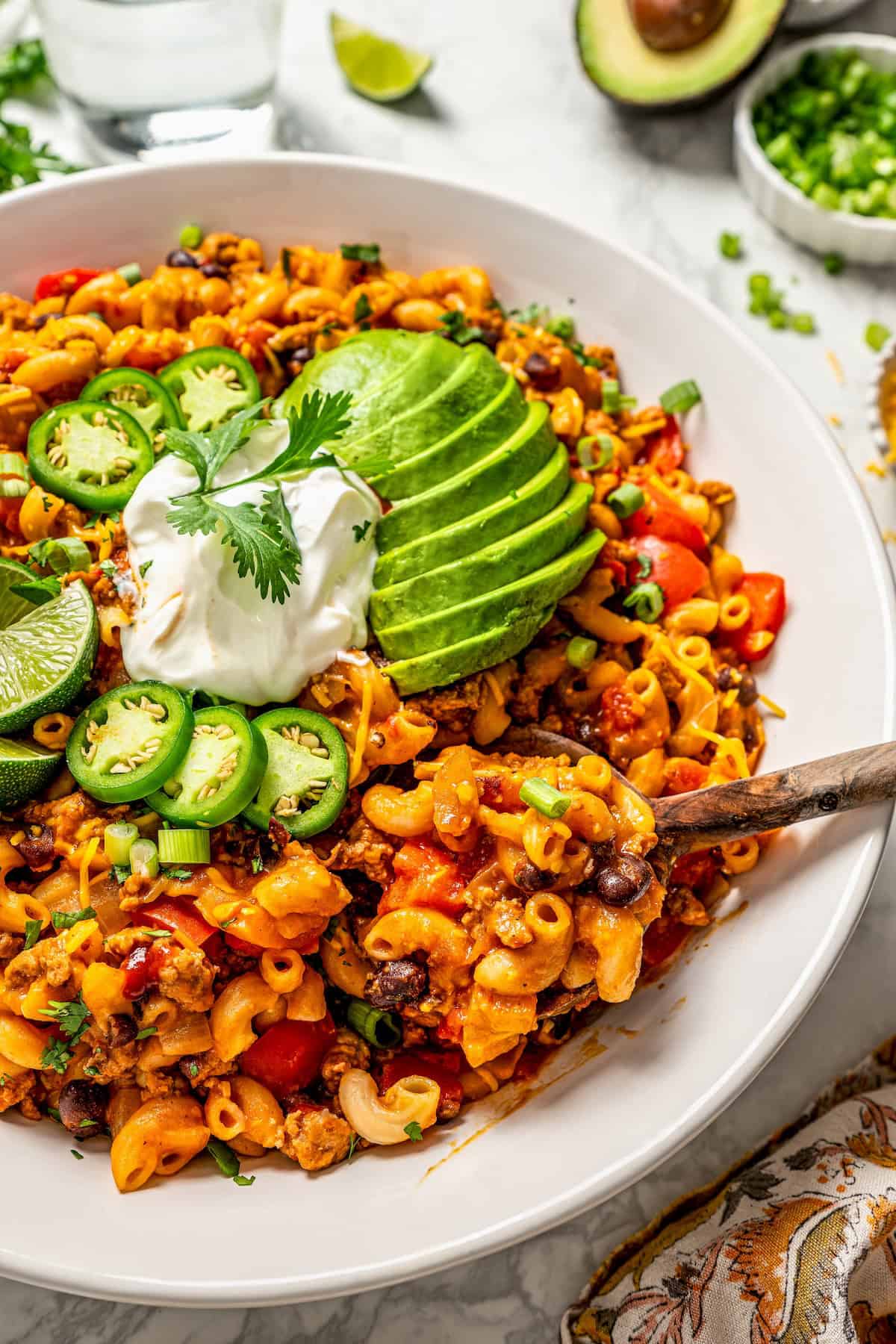 A wooden spoon scooping up some taco pasta from a large white serving bowl.