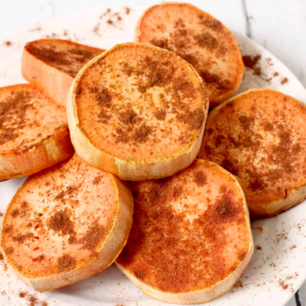 Sliced rounds of roasted sweet potatoes arranged on a plate with cinnamon sprinkled on top.