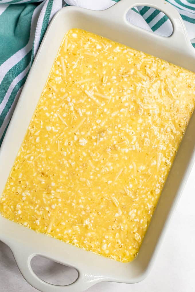 A white rectangular casserole dish with an unbaked egg and cheese mixture poured in.
